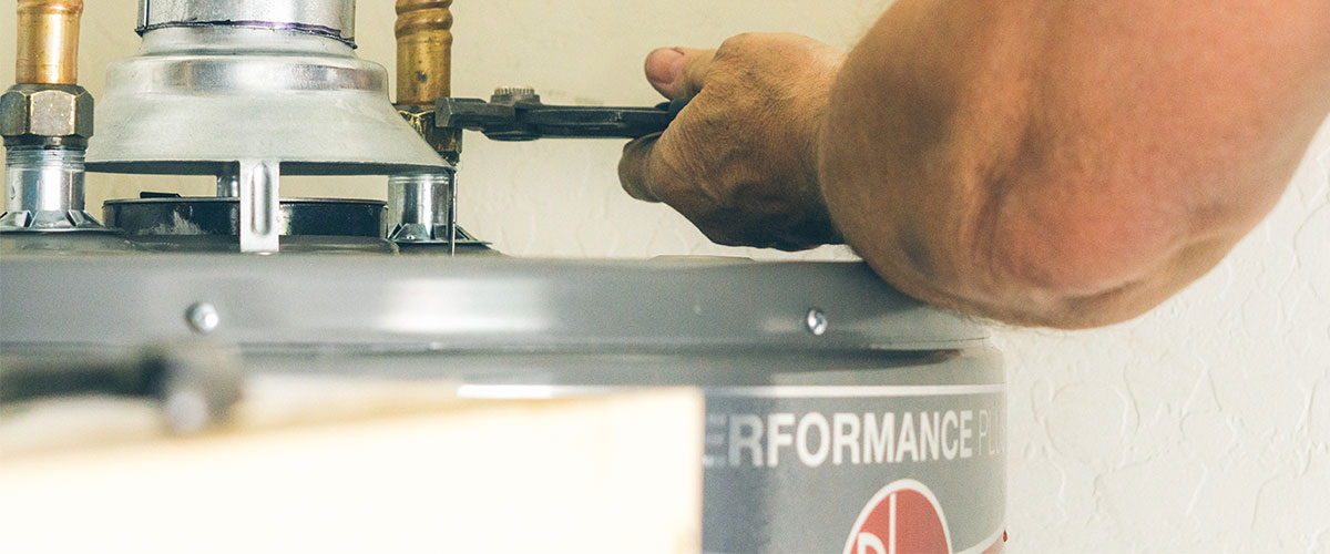 Man working on a traditional water heater vs a tankless one